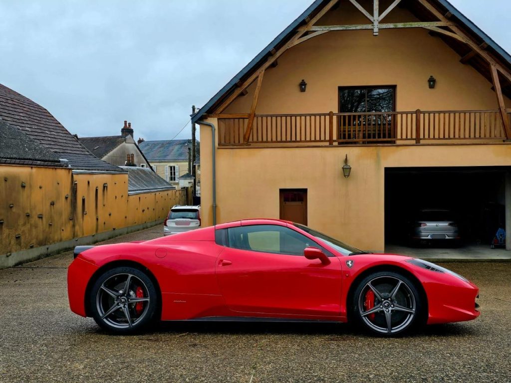 Une Ferrari rouge de profil devant une maison.